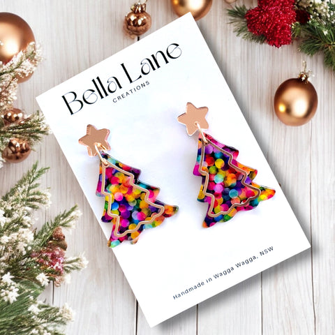 Colorful Christmas tree-shaped earrings on a Bella Lane card with festive decorations.